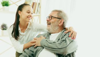 A daughter or granddaughter spends time with the grandfather or senior man. Family or fathers' day, positive emotions and happieness. Lifestyle portrait at home. Two people caddling and smiling.